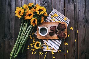 mug of coffee, brownies, sunflowers, wood board, napkin on wood table
